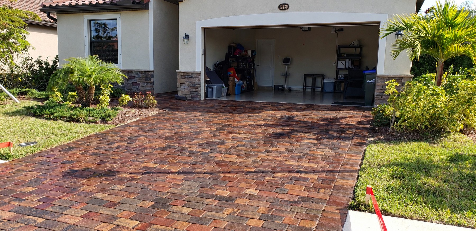 Residential driveway pavers framed by palms and a planted garden