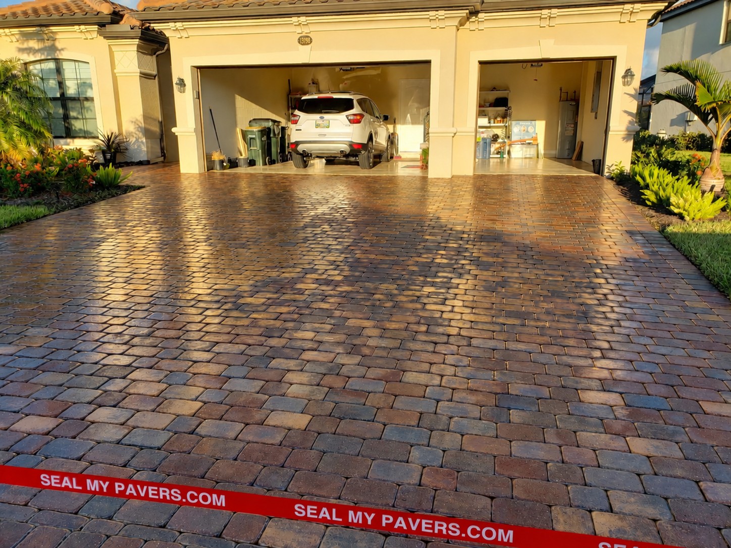 After view of dark driveway pavers with a white vehicle in the open garage
