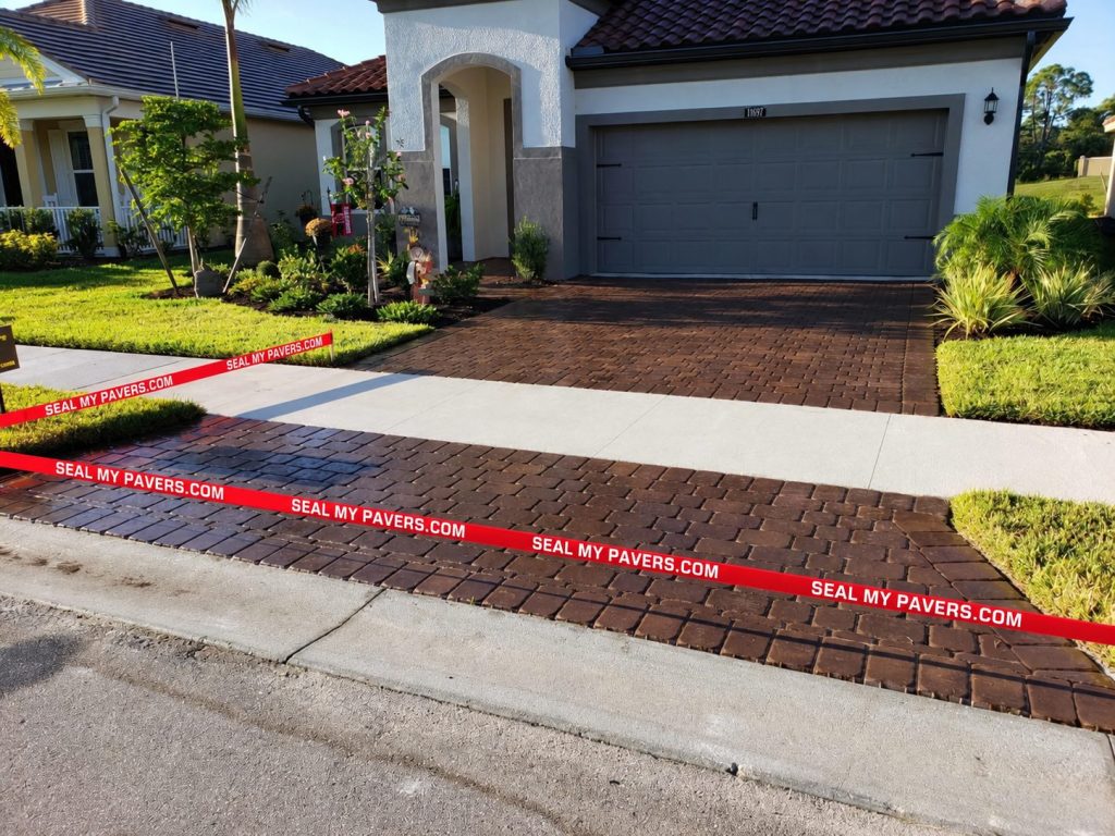 Brown paver driveway with a sidewalk crossing and red Seal My Pavers tape on Renaissance Drive