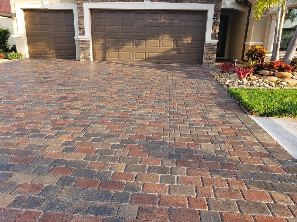 Red, tan, and gray driveway pavers leading to two dark garage doors on Famiglia Drive