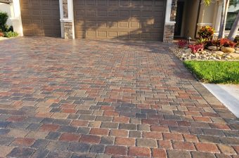 Red, tan, and gray driveway pavers leading to two dark garage doors on Famiglia Drive