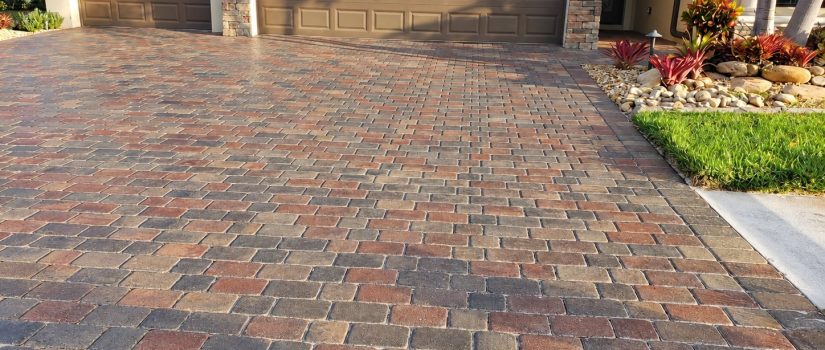 Red, tan, and gray driveway pavers leading to two dark garage doors on Famiglia Drive