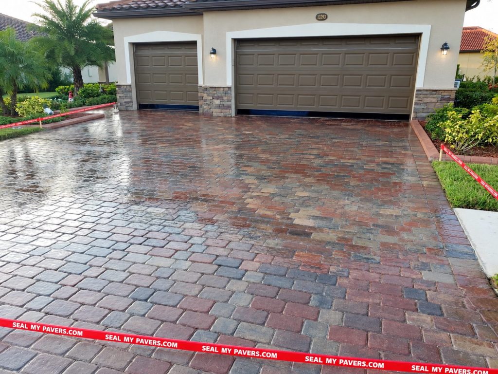 Reflective red and gray paver driveway in front of two brown garage doors on Famiglia Drive