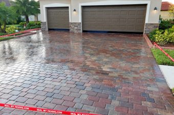 Reflective red and gray paver driveway in front of two brown garage doors on Famiglia Drive