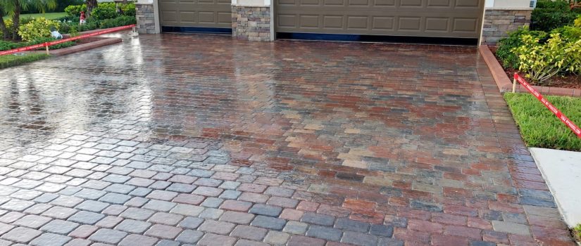 Reflective red and gray paver driveway in front of two brown garage doors on Famiglia Drive