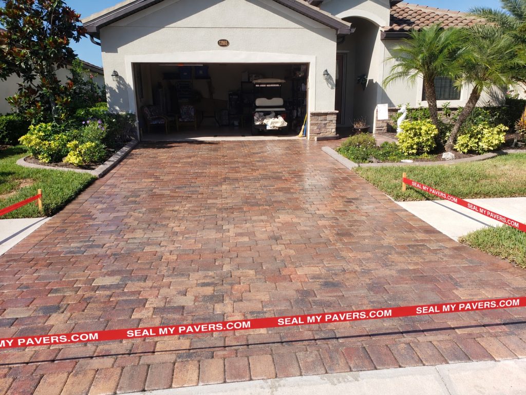 Warm-toned paver driveway leading to an open garage, with red barrier tape across the entrance