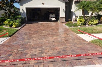 Warm-toned paver driveway leading to an open garage, with red barrier tape across the entrance