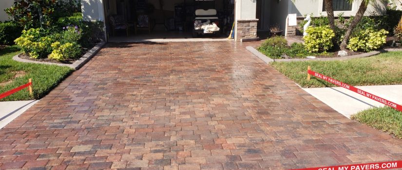 Paver driveway cleaned and sealed by Seal My Pavers, with neatly straightened red branded barrier tape.